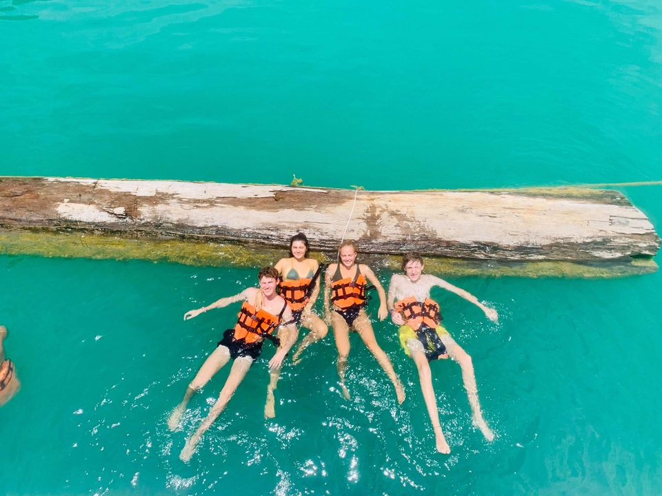 People floating with life vests on a log in turquoise water.