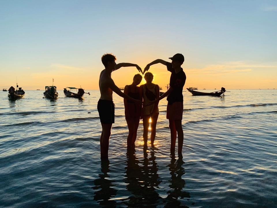 People standing in shallow water at sunset forming a heart shape.