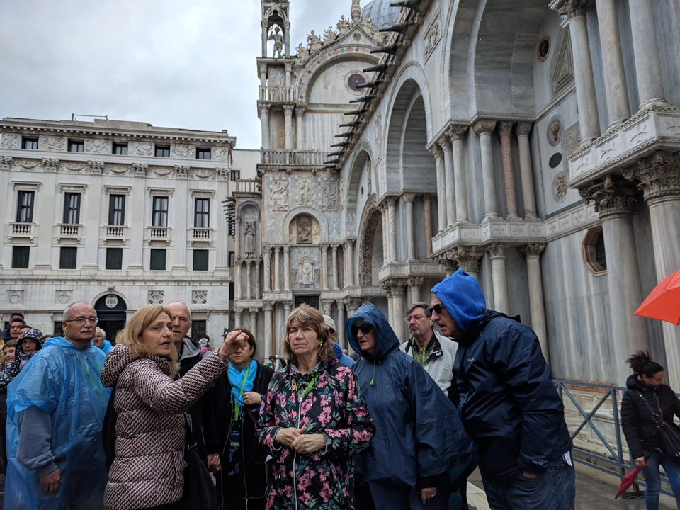 Groupe de touristes portant des imperméables devant un bâtiment historique.