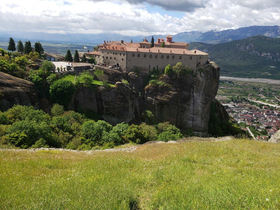 Monastère perché au sommet d'une falaise rocheuse avec une vallée verdoyante en contrebas.