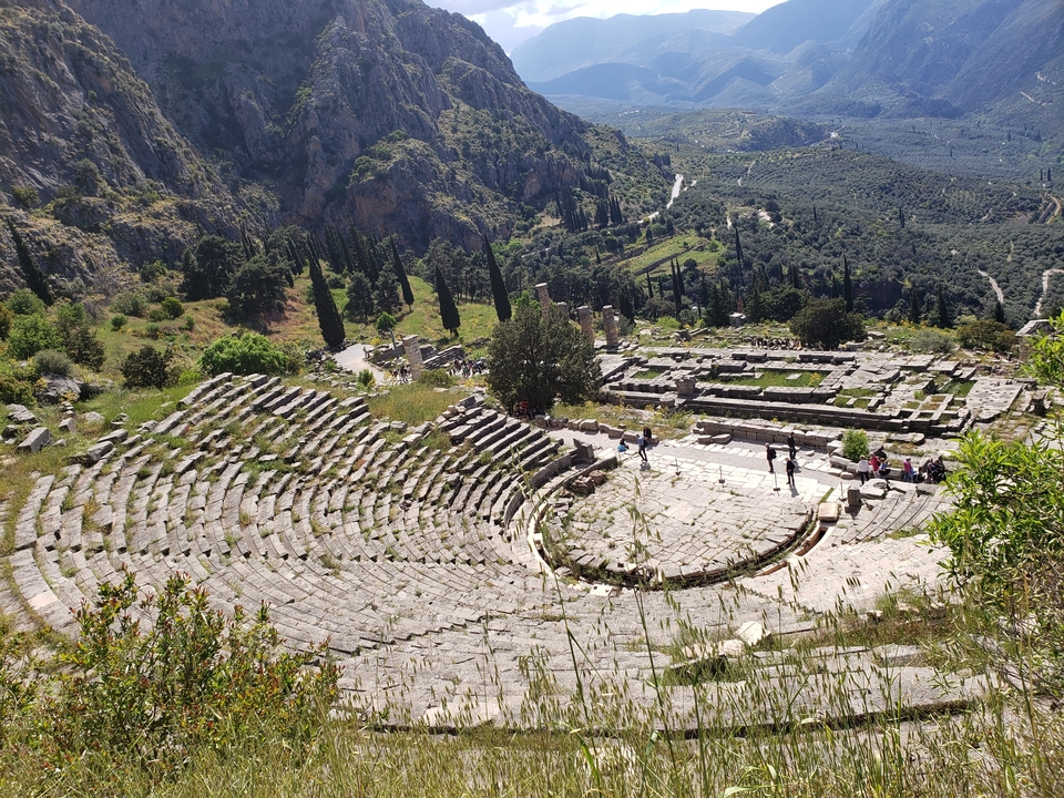 Ancien amphithéâtre de pierre entouré d'arbres et de montagnes.