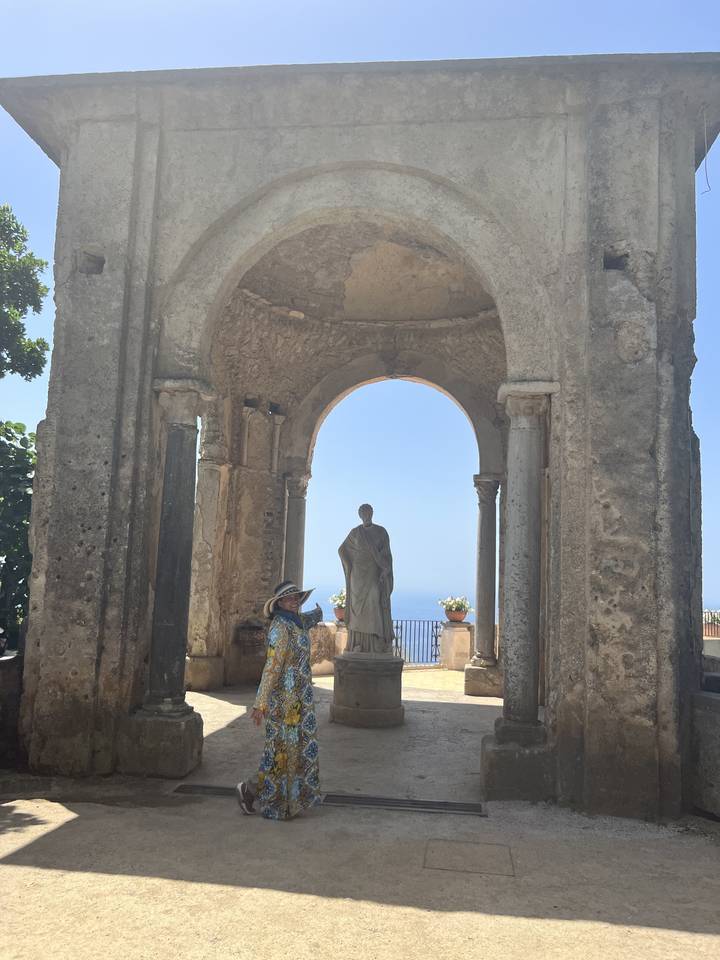 Personne debout dans une arche historique avec une statue et un ciel bleu visible.