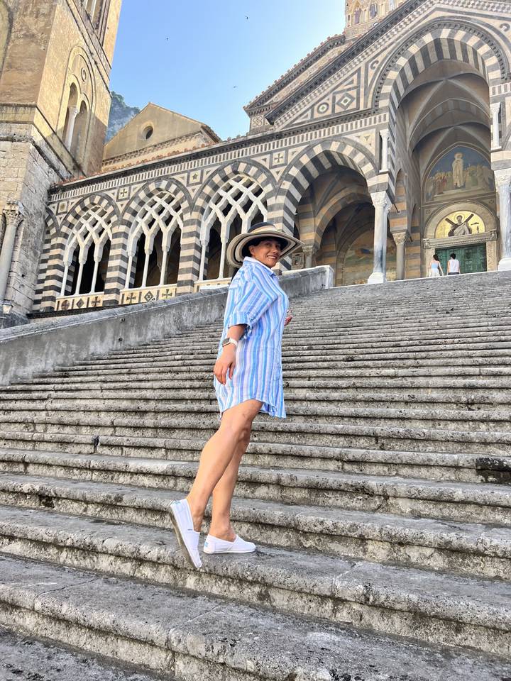 Personne en robe rayée posant sur des escaliers architecturaux.