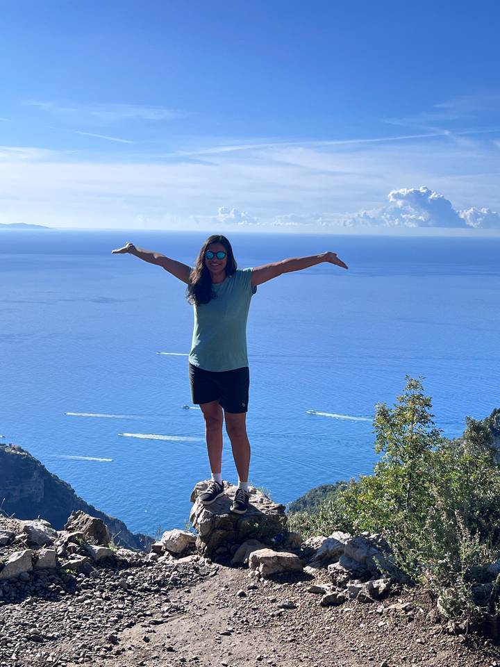 Personne posant avec les bras étendus au-dessus d'une vue côtière.