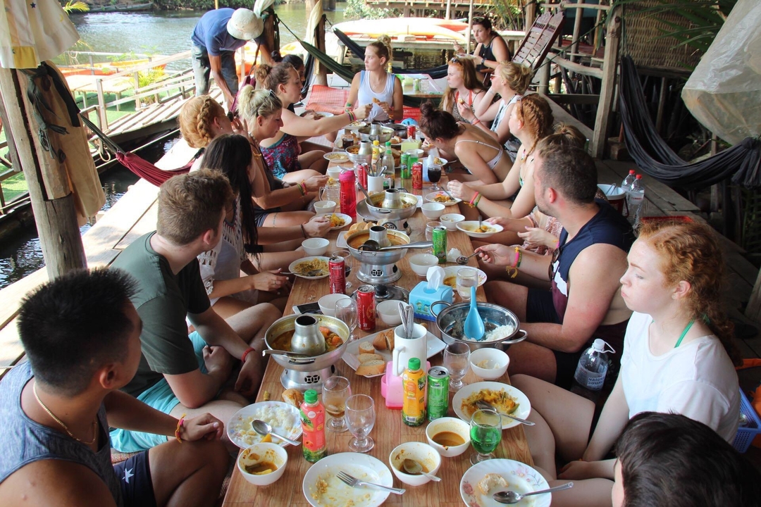 Grand groupe dînant ensemble sur une terrasse au-dessus de l'eau.