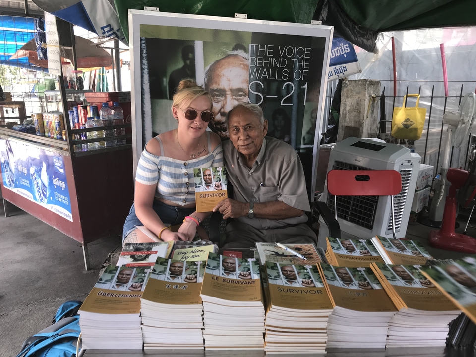 Femme assise avec un homme âgé à un étal de livres.