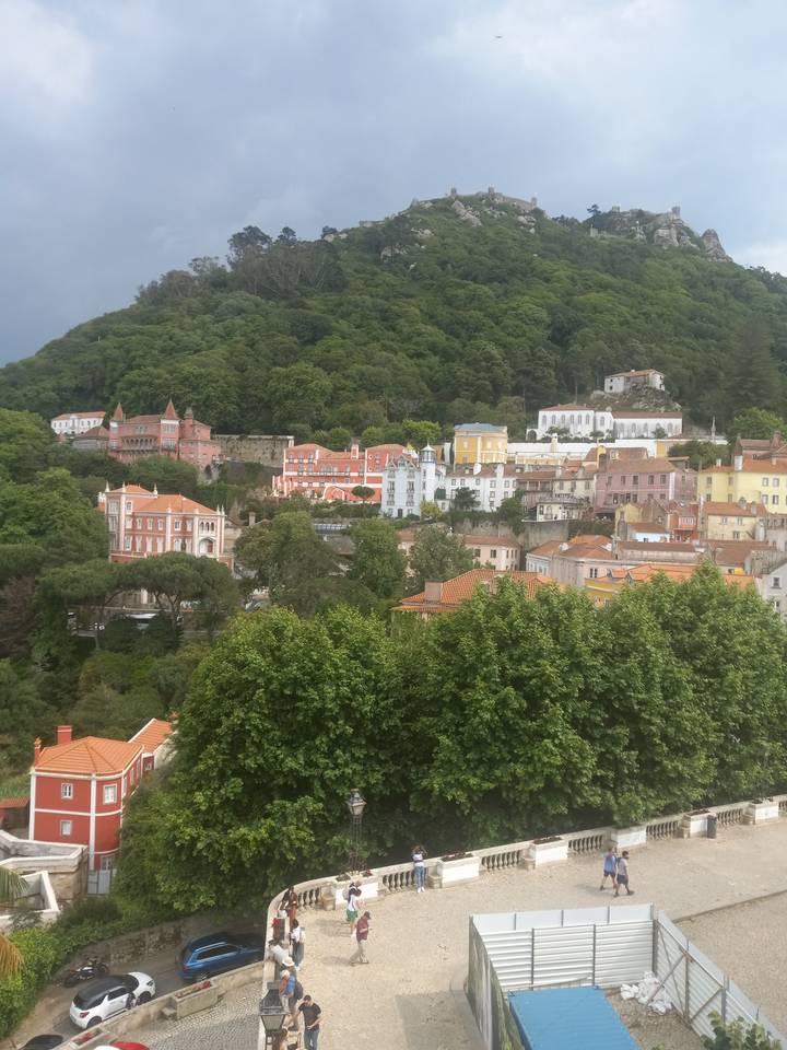 Des gens sur une plateforme observent une ville historique entourée de collines.