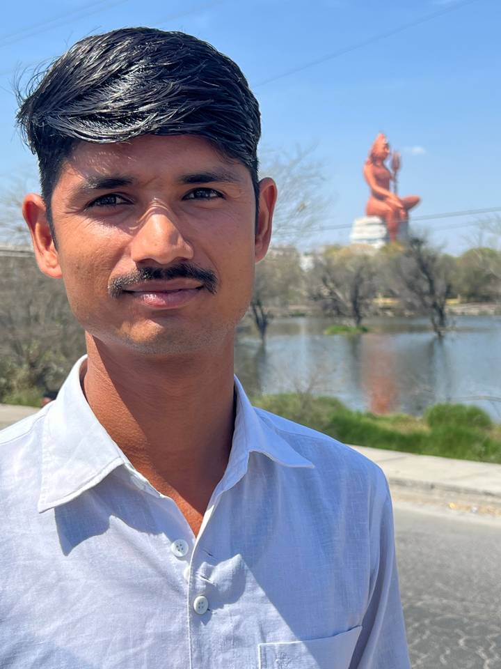 Un homme posant près d'une statue avec un décor aquatique en arrière-plan.