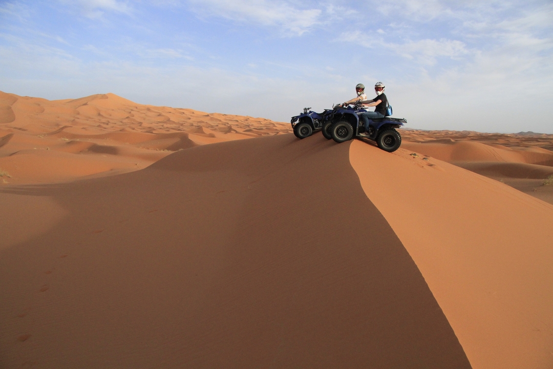 Deux personnes sur des VTT sur une dune de sable dans un paysage désertique.