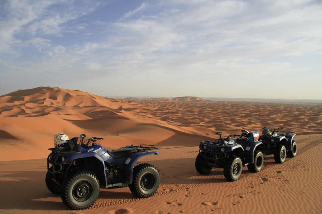 Trois VTT stationnés sur un vaste paysage de dunes désertiques.