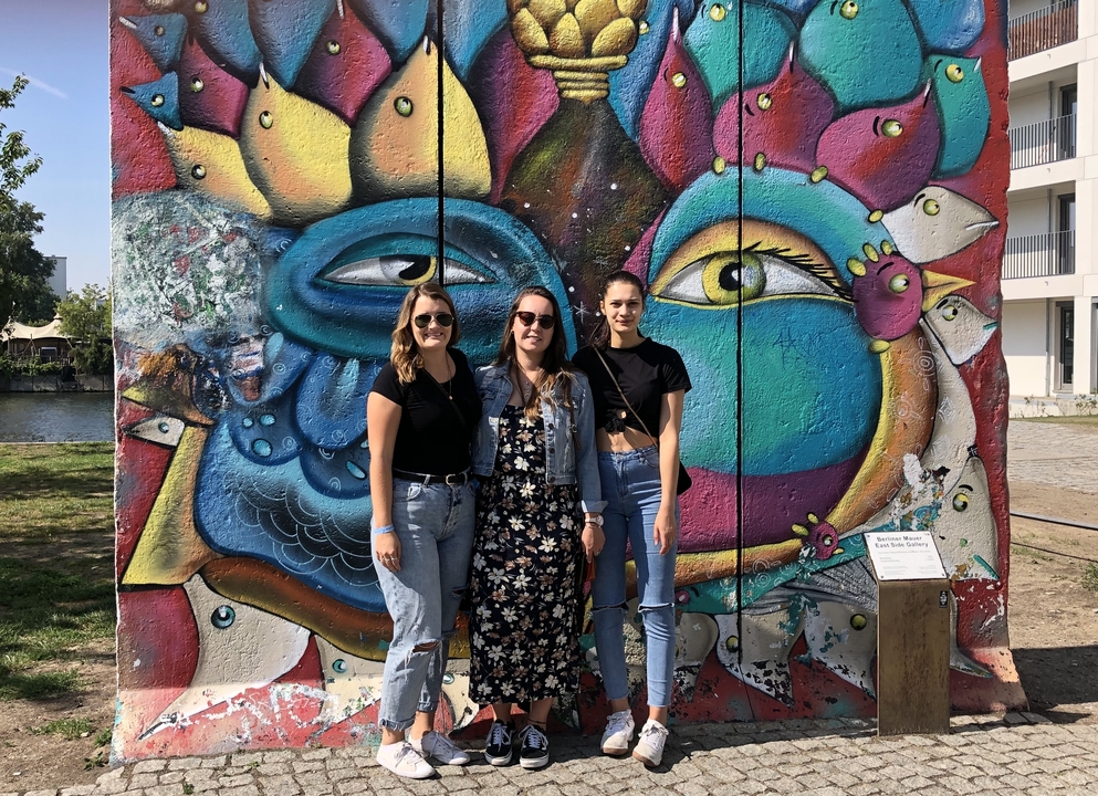 Trois femmes debout devant une peinture murale colorée.