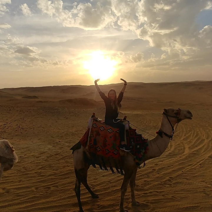 Personne chevauchant un chameau dans le désert au coucher du soleil.