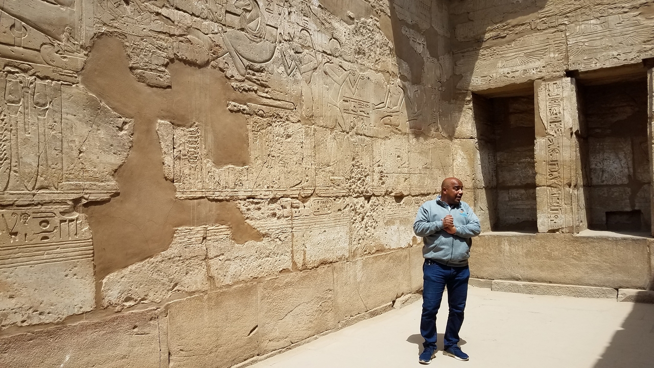 Homme debout devant un mur égyptien antique avec des hiéroglyphes.