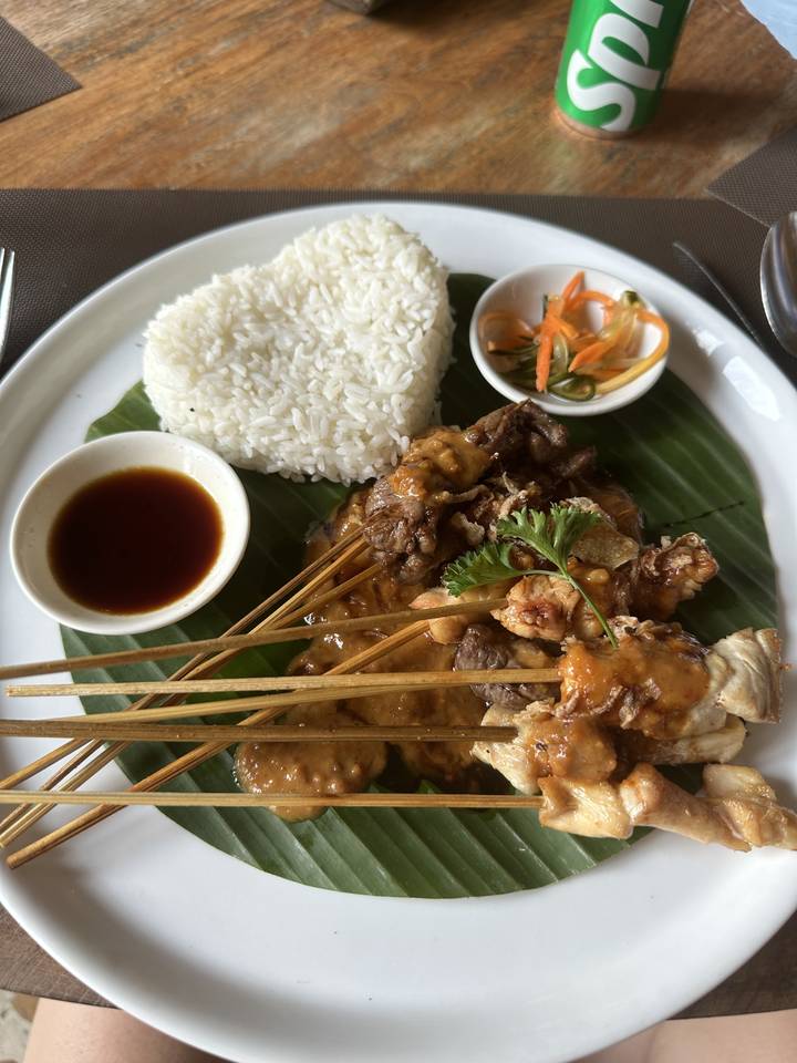 A plate of satay with rice and sauce on a leaf.