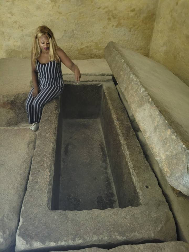 Personne accroupie près d'un sarcophage de pierre ancien.
