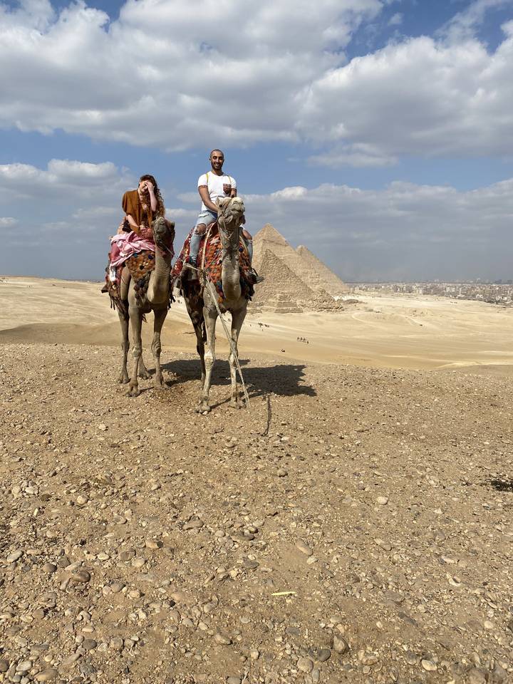 Des gens à dos de chameau avec des pyramides en arrière-plan.