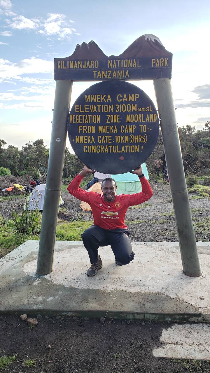 Homme posant avec un panneau du Parc National du Kilimandjaro