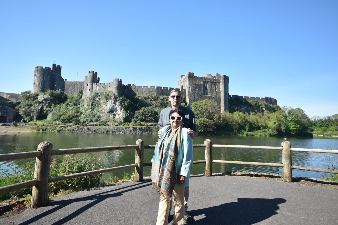 Deux personnes posant devant le château de Pembroke avec un reflet dans l'eau.