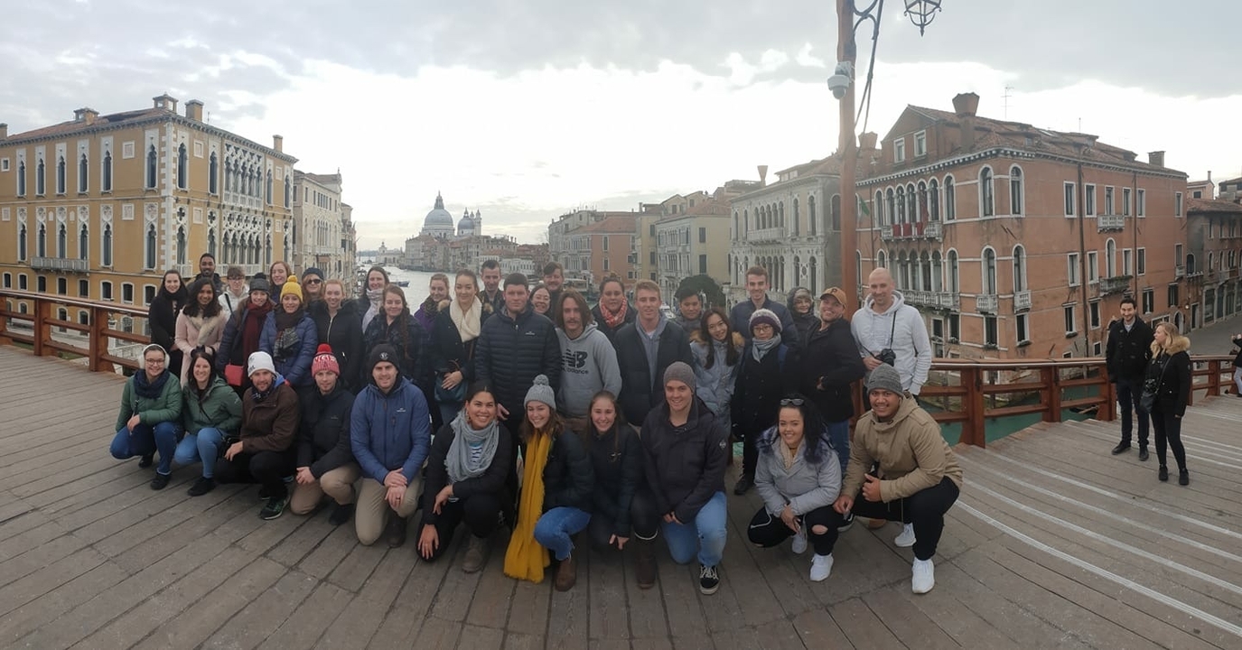Grand groupe de touristes posant sur un pont avec vue sur un canal.