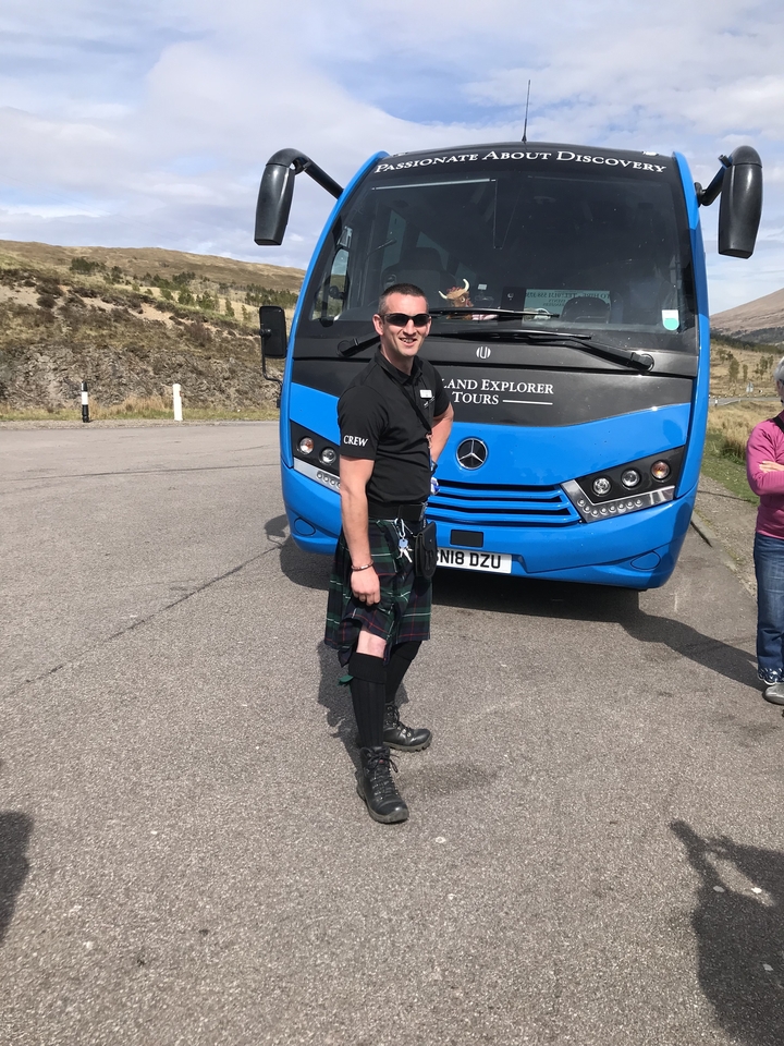 Homme en kilt debout devant un autocar de tourisme.