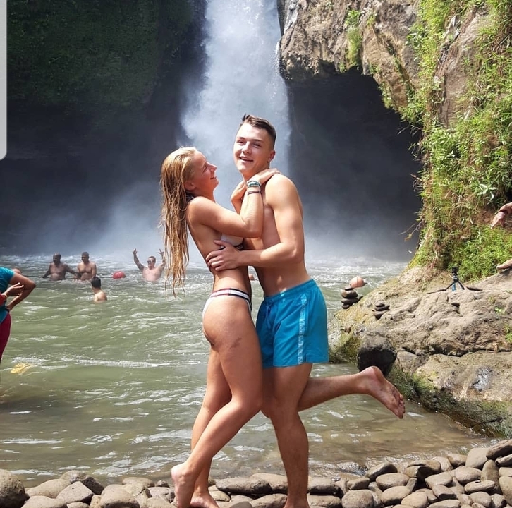 Couple embracing near a waterfall with people in the background.