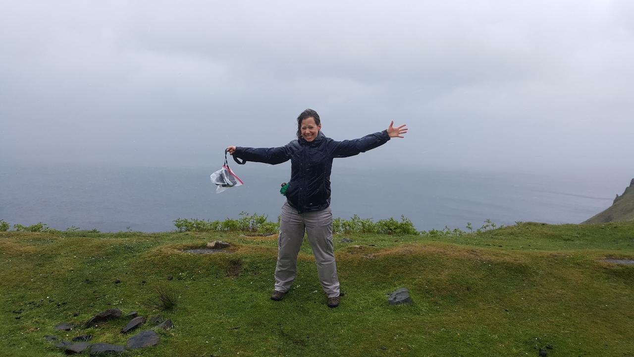 A person poses happily on a hill in windy weather.