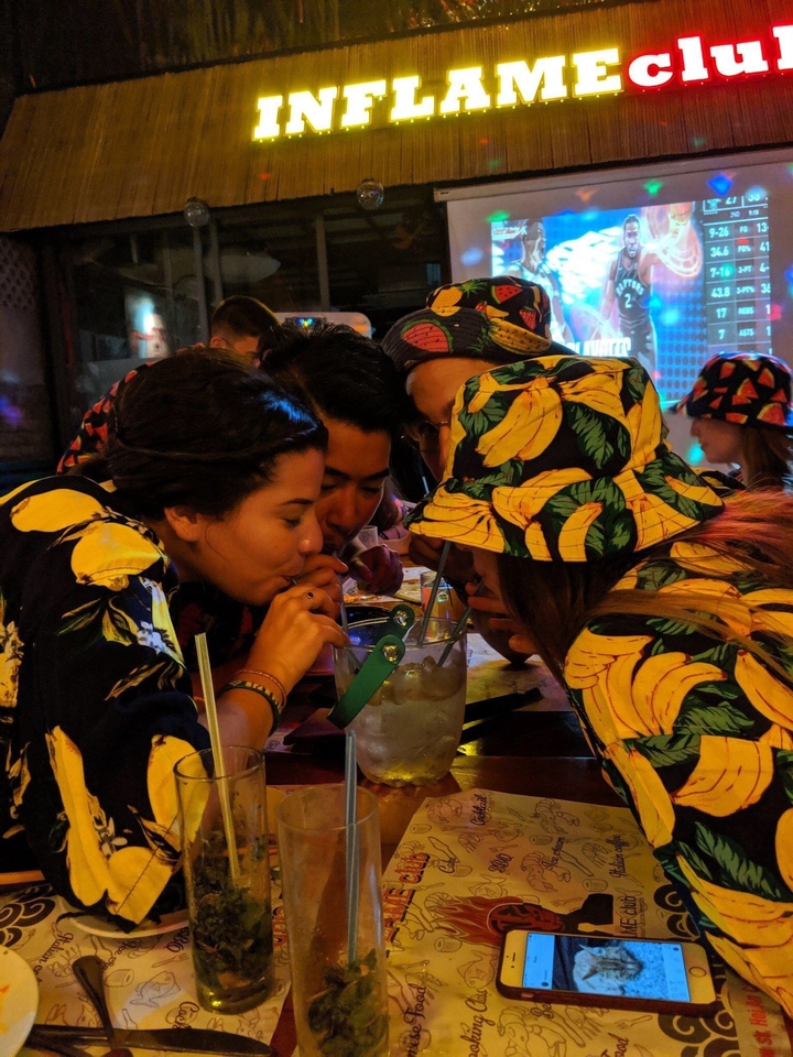 Groupe de personnes buvant dans un récipient partagé à l'intérieur la nuit.