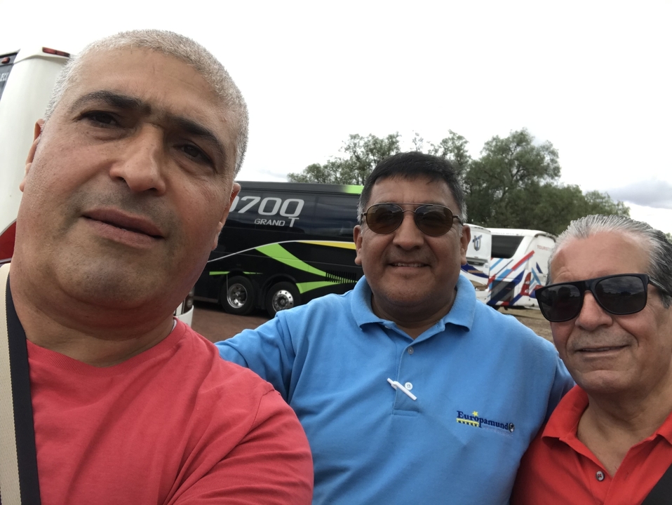 Trois personnes qui sourient devant des autocars de tourisme stationnés.