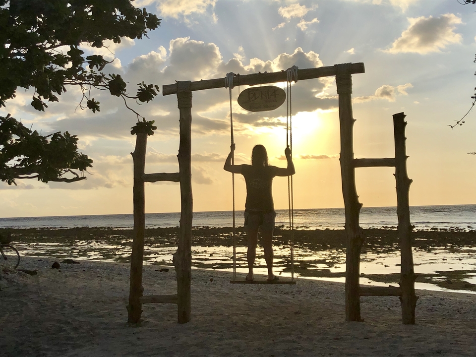 Silhouette d'une personne sur une balançoire face à l'océan au coucher du soleil.