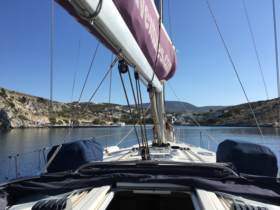 Voilier entrant dans une baie avec des maisons sur les collines.