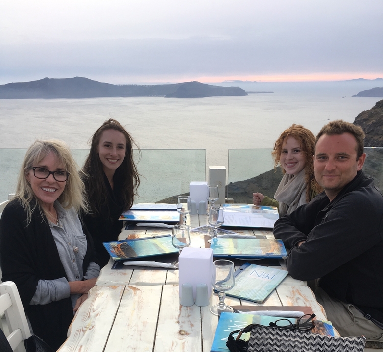 Quatre personnes dînant avec une vue panoramique sur la mer au coucher du soleil.