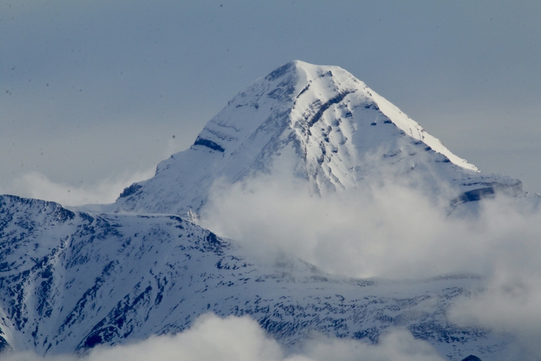 Un sommet montagneux proéminent couronné de neige, partiellement voilé de nuages.