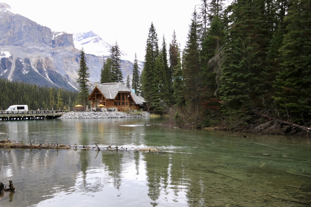 Une cabane rustique au bord d'un lac entourée de forêt et de montagnes.