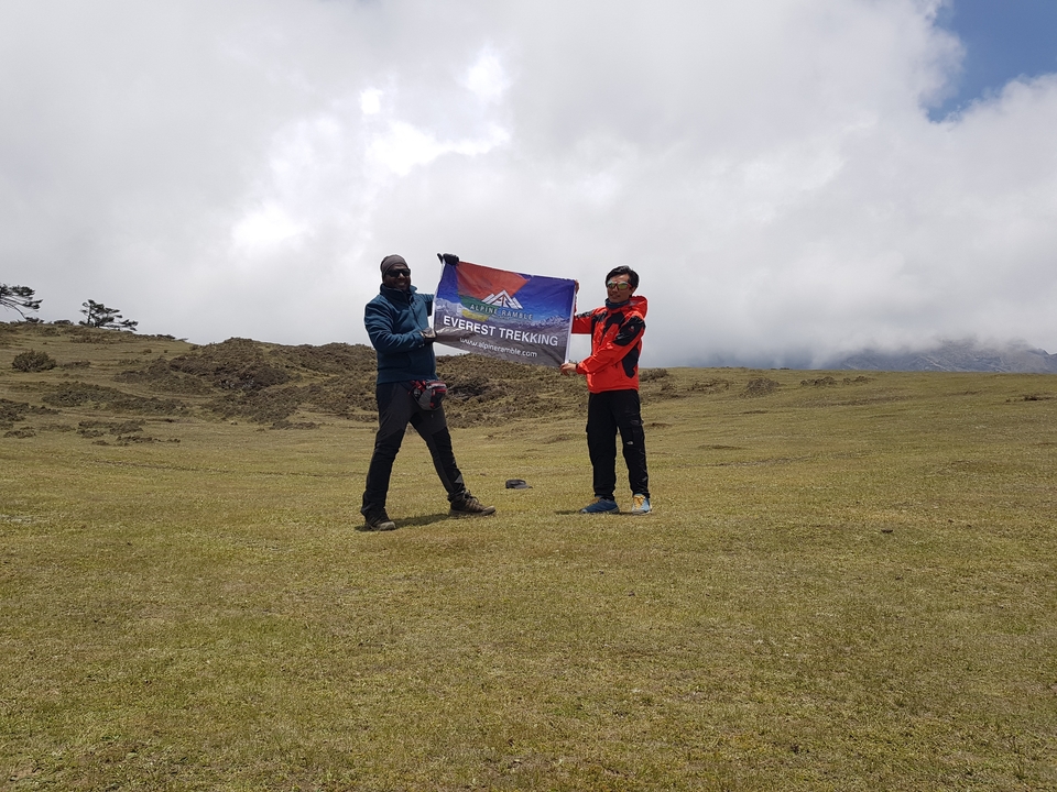 Deux personnes tenant un drapeau dans une zone herbeuse avec un ciel nuageux.