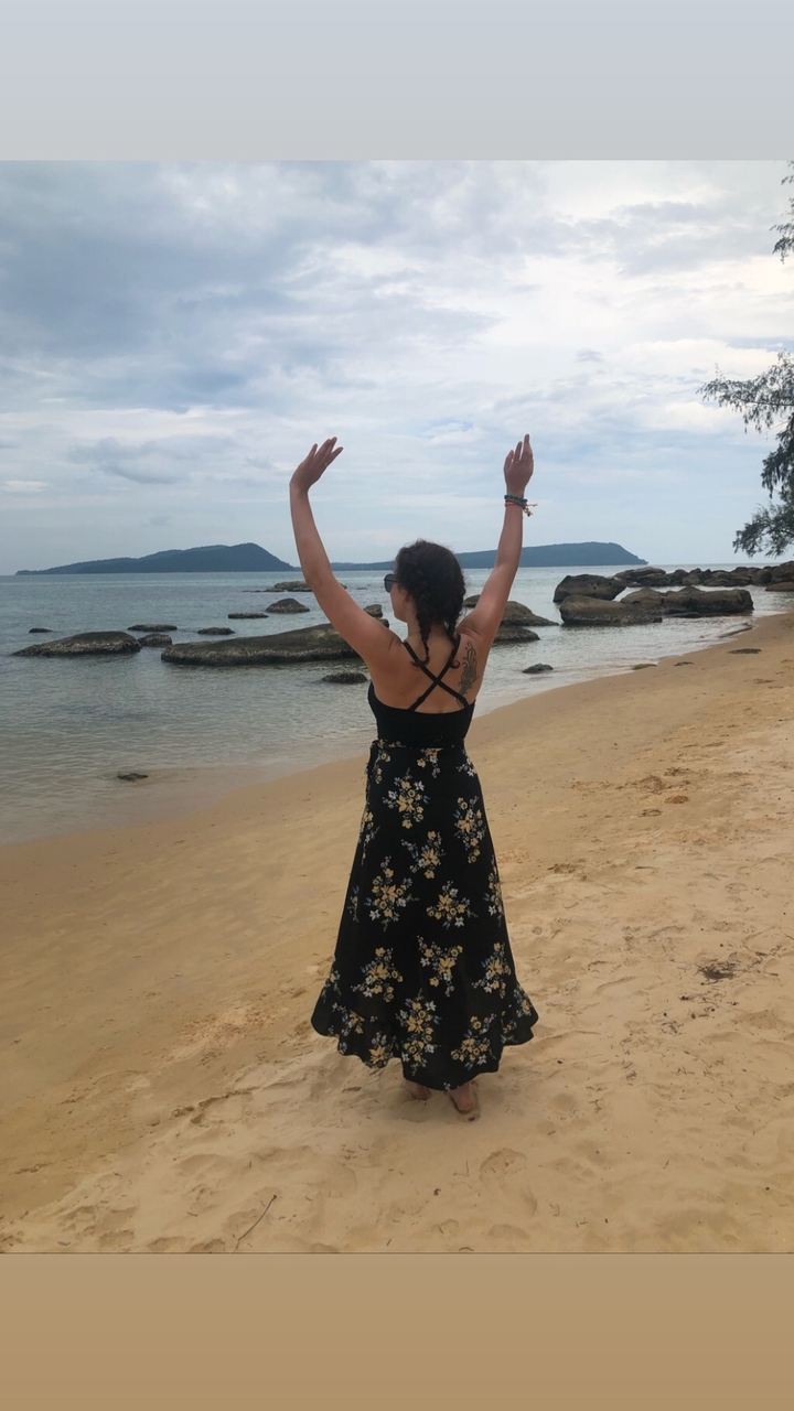 Back view of a woman raising her arms on a sandy beach.