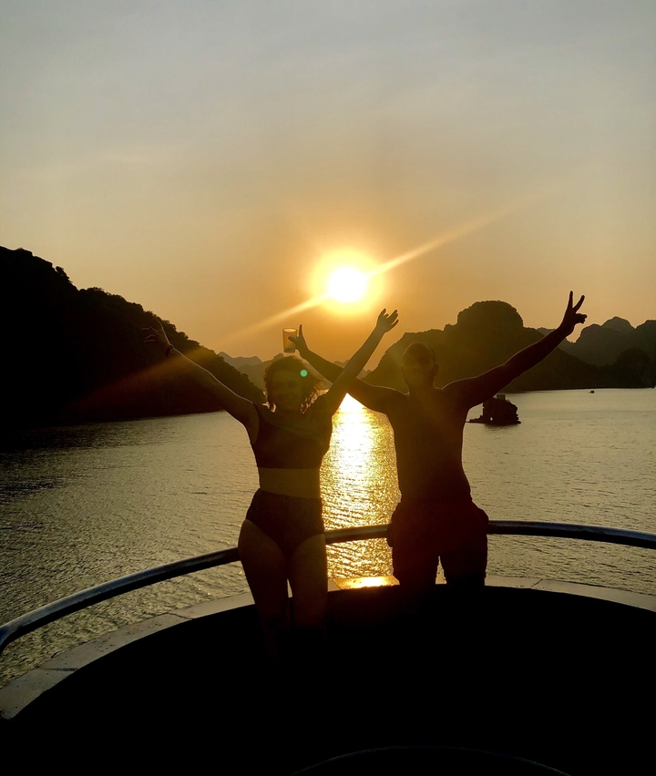Two people raising their arms on a boat at sunset.