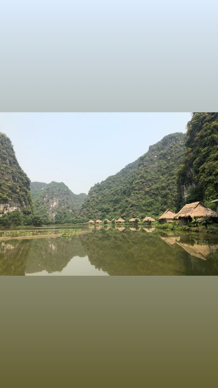 Huts along a lake surrounded by lush green hills.