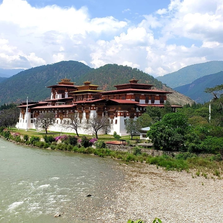 Un grand bâtiment traditionnel bhoutanais, probablement le Punakha Dzong, avec une rivière au premier plan.