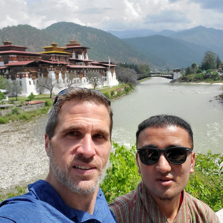Deux individus souriants avec le Punakha Dzong et une rivière en arrière-plan.