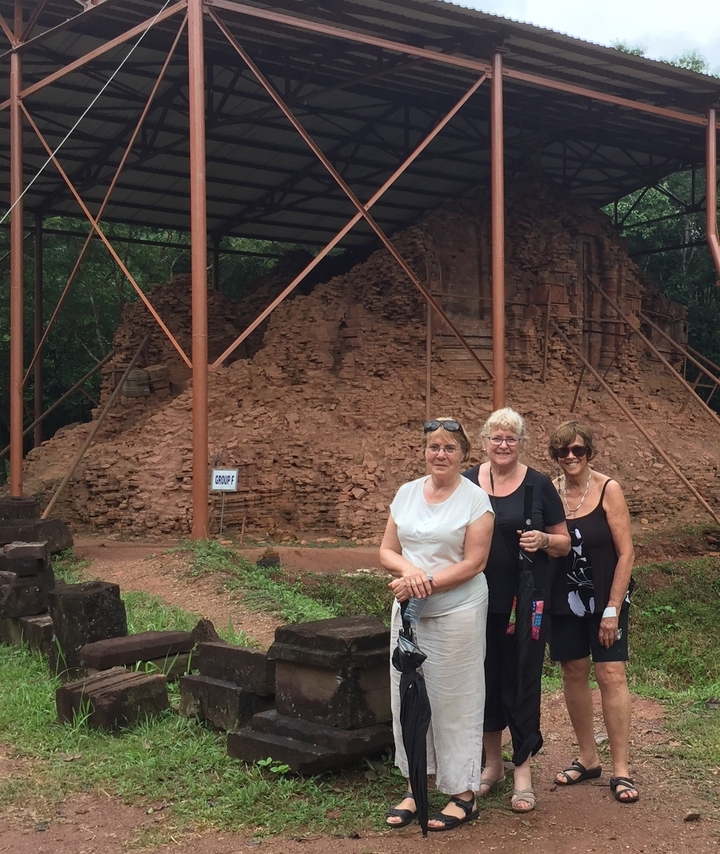 Trois femmes devant une structure de ruine antique en briques.