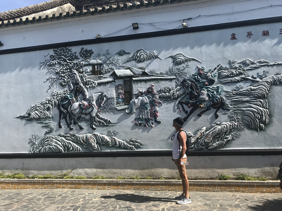 Homme regardant une œuvre d'art murale complexe représentant des scènes historiques.