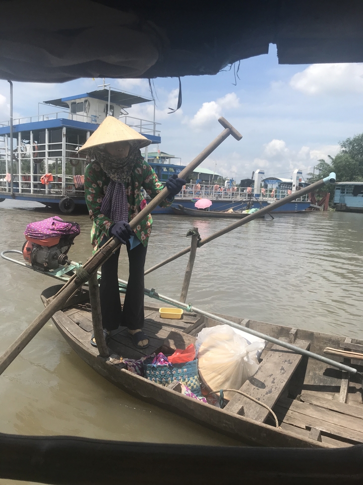 Personne ramant dans un petit bateau sur une rivière avec d'autres bateaux en arrière-plan.