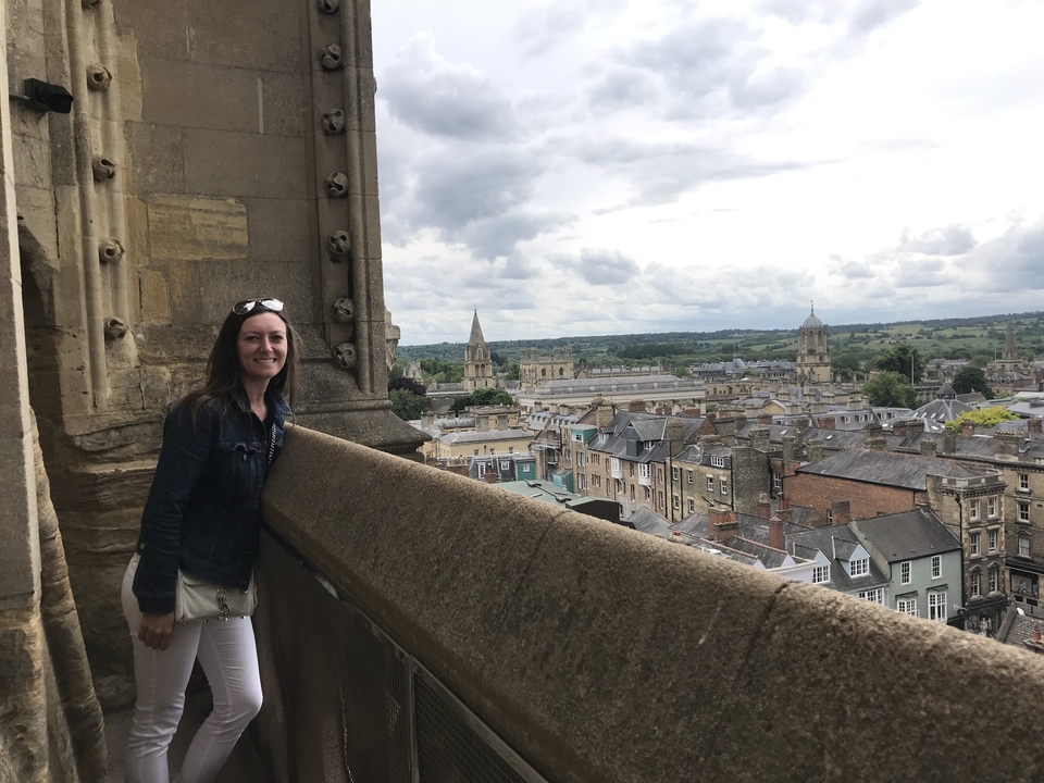 Femme sur un balcon donnant sur un paysage urbain avec des bâtiments historiques.