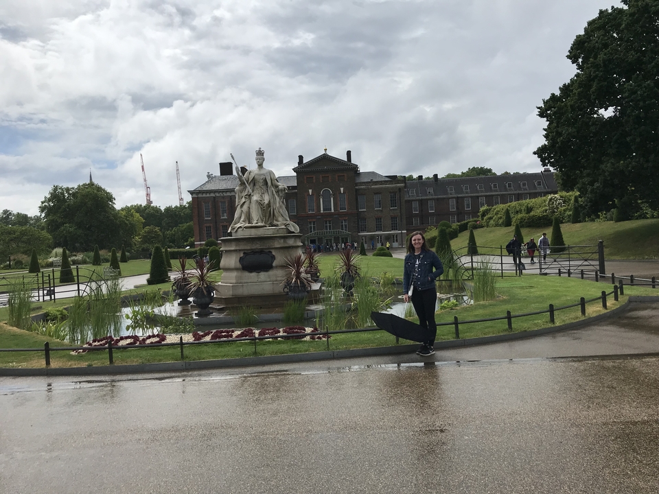 Personne tenant un parapluie devant une statue historique et un bâtiment dans un parc.