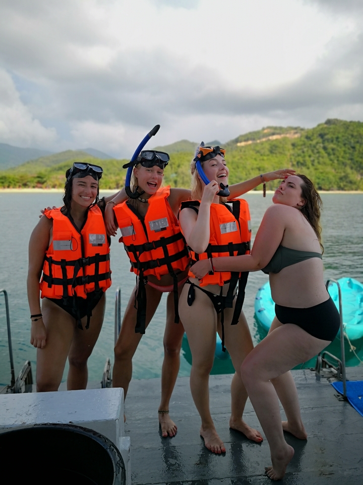 Friends posing with life jackets, near a boat.