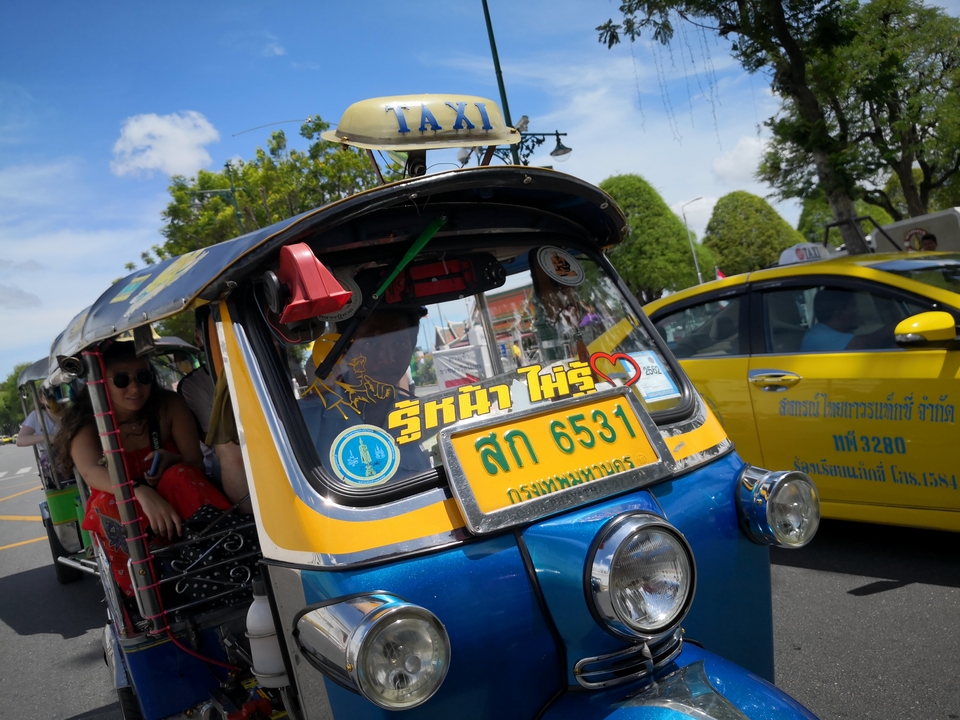 Colorful tuk-tuk taxi with passenger inside, city street setting.