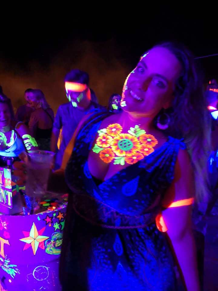 Person holding a drink at a glow party with colorful lights.