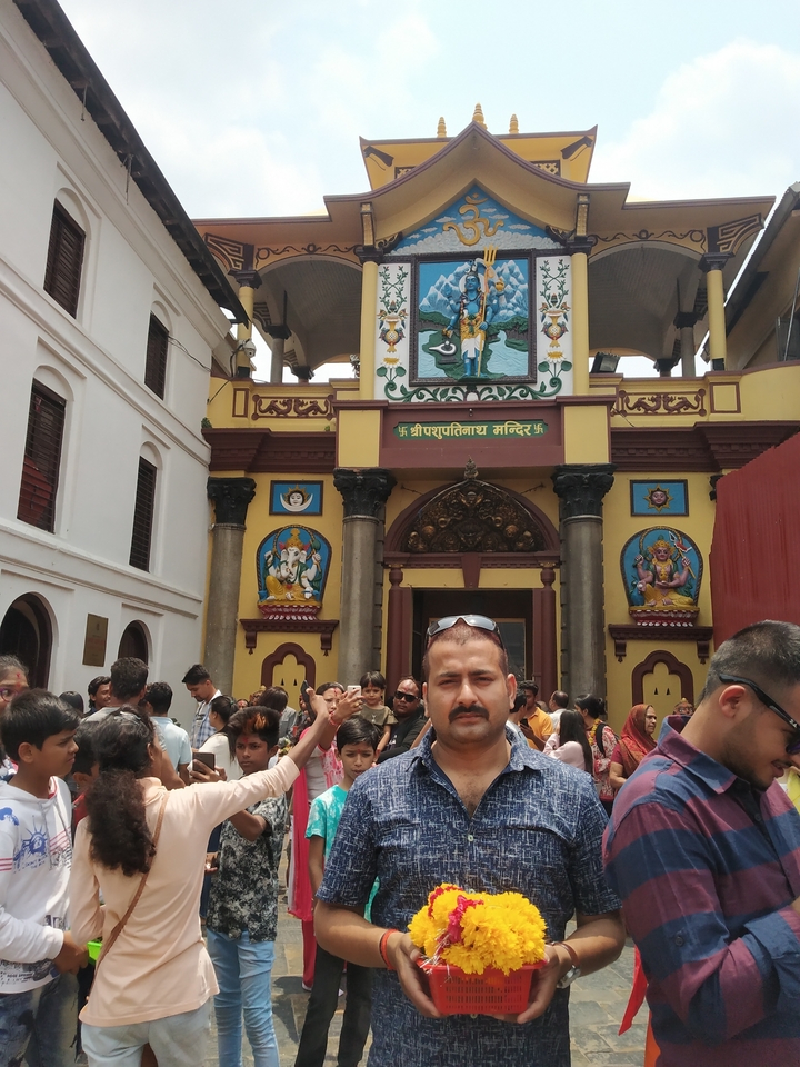 Crowds gather outside an ornate yellow and brown Hindu temple with colourful deity carvings in Nepal.