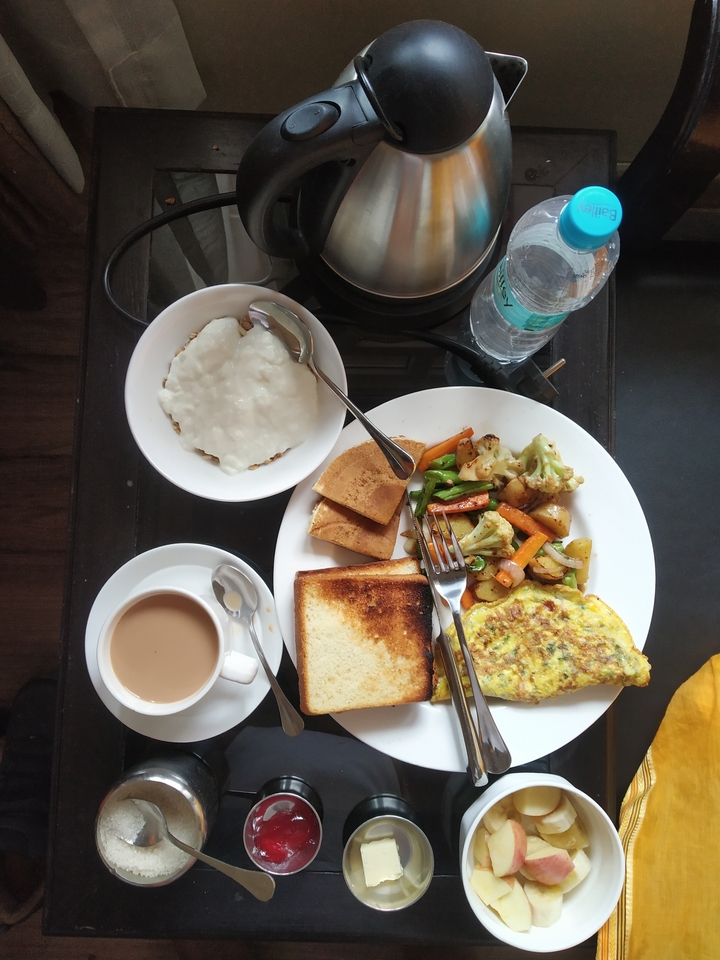 A neatly arranged breakfast with toast, omelette, sautéed vegetables, porridge and a cup of tea on a glass-top table.