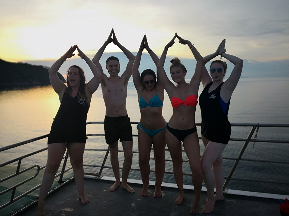 Group posing on a boat with sunset in the background.